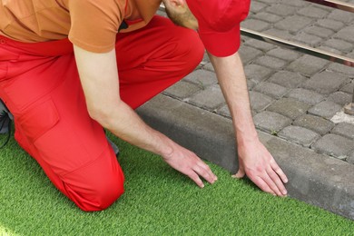 Photo of Man in uniform installing artificial turf outdoors, closeup