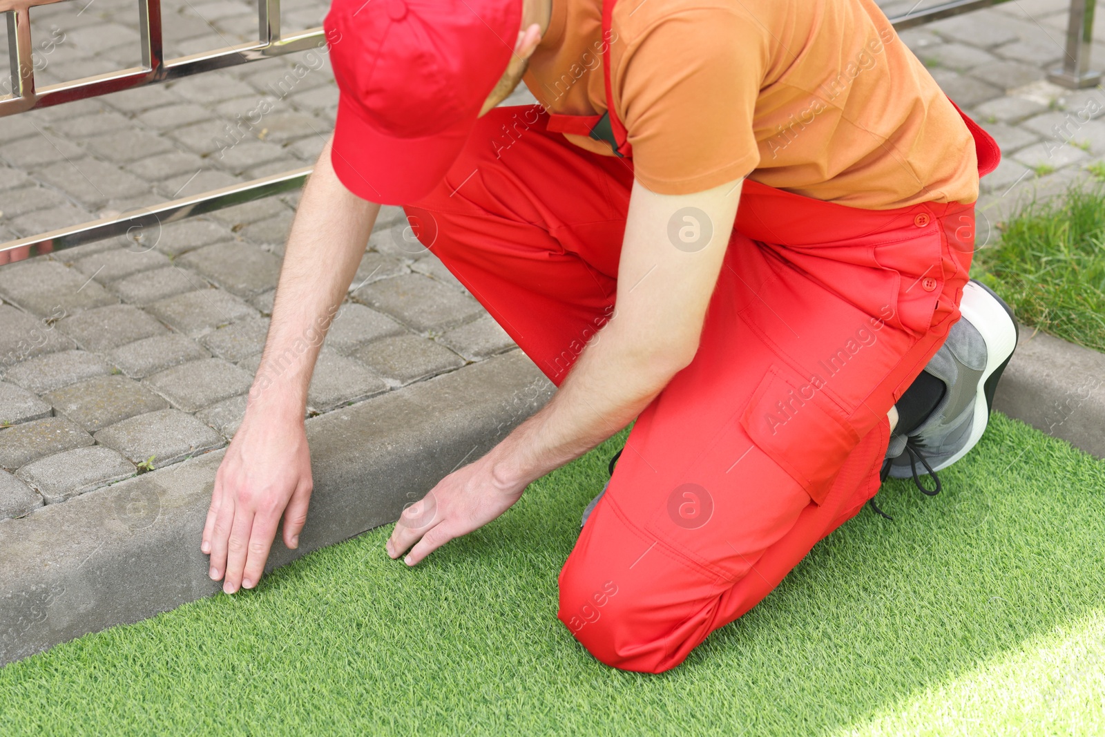 Photo of Man in uniform installing artificial turf outdoors, closeup