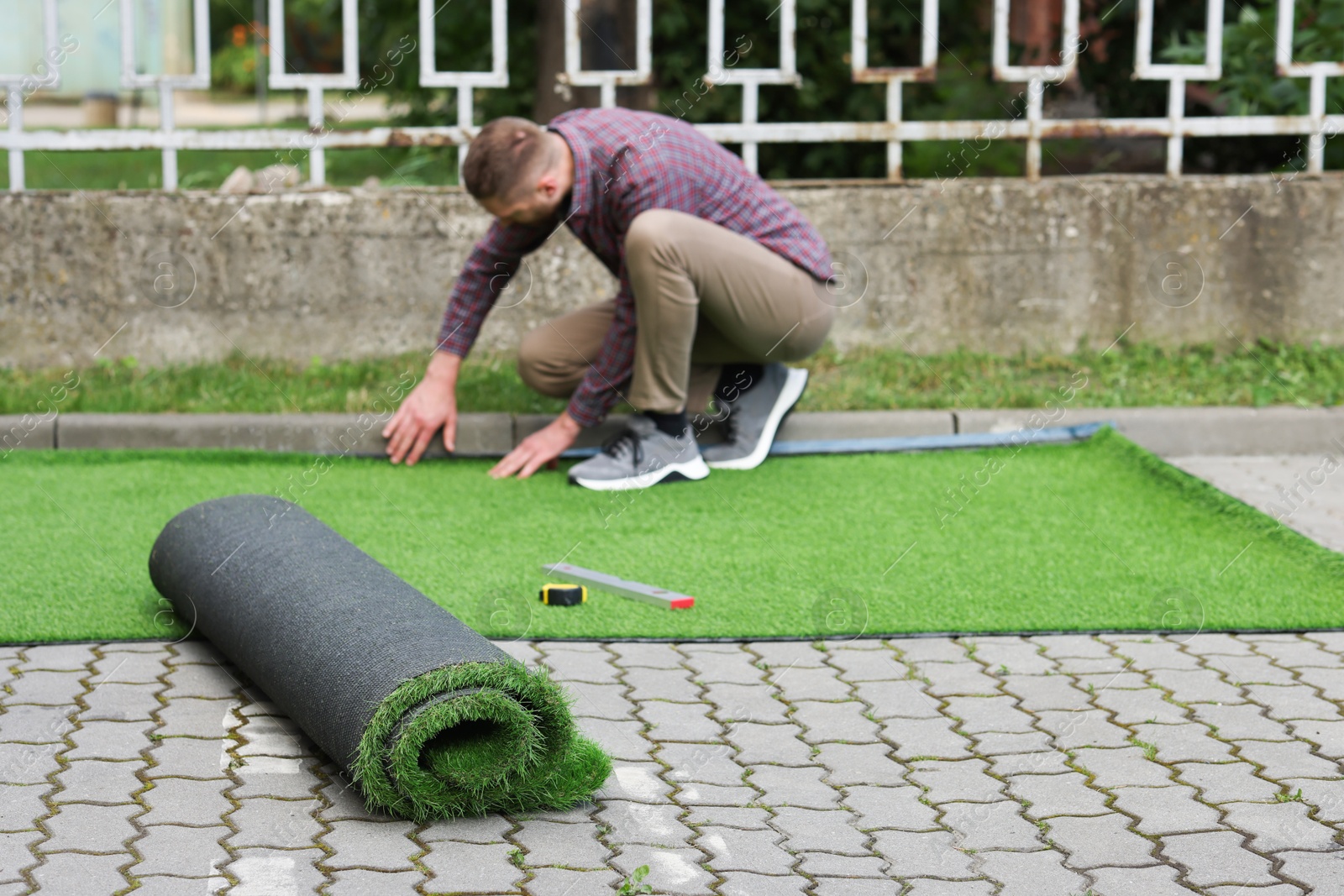 Photo of Young man installing artificial turf outdoors, selective focus