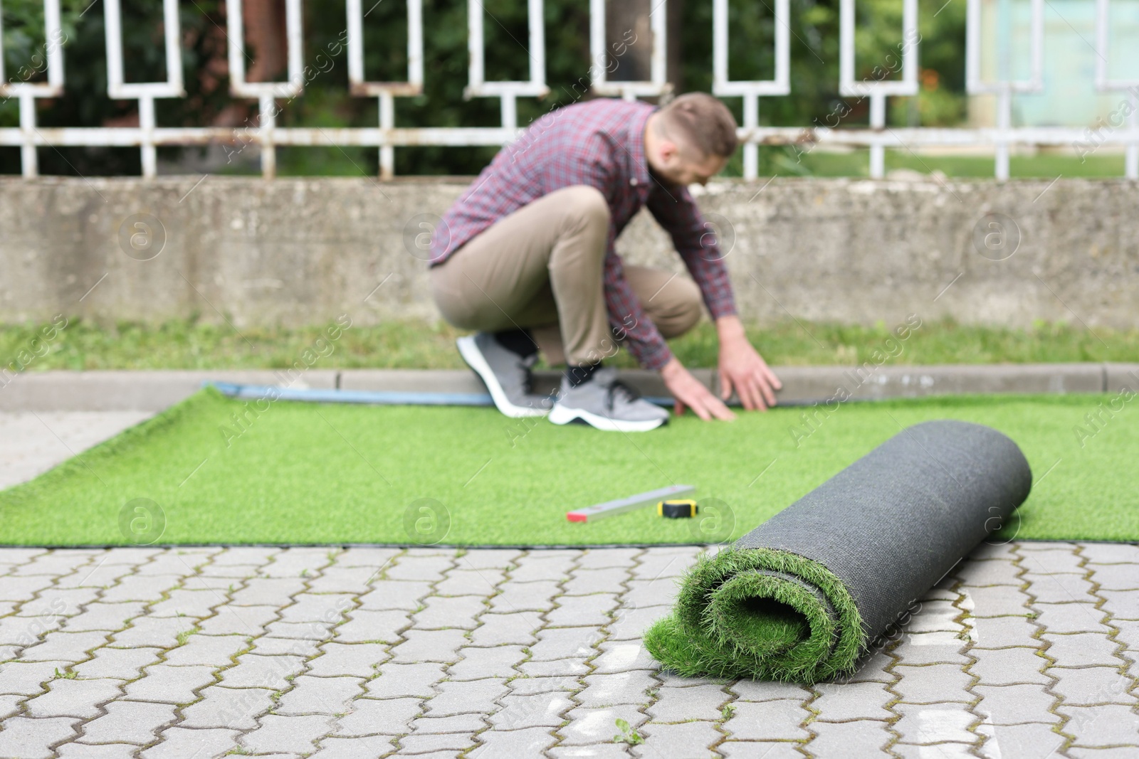 Photo of Young man installing artificial turf outdoors, selective focus