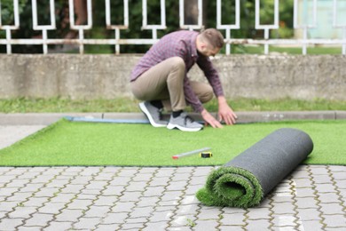 Young man installing artificial turf outdoors, selective focus