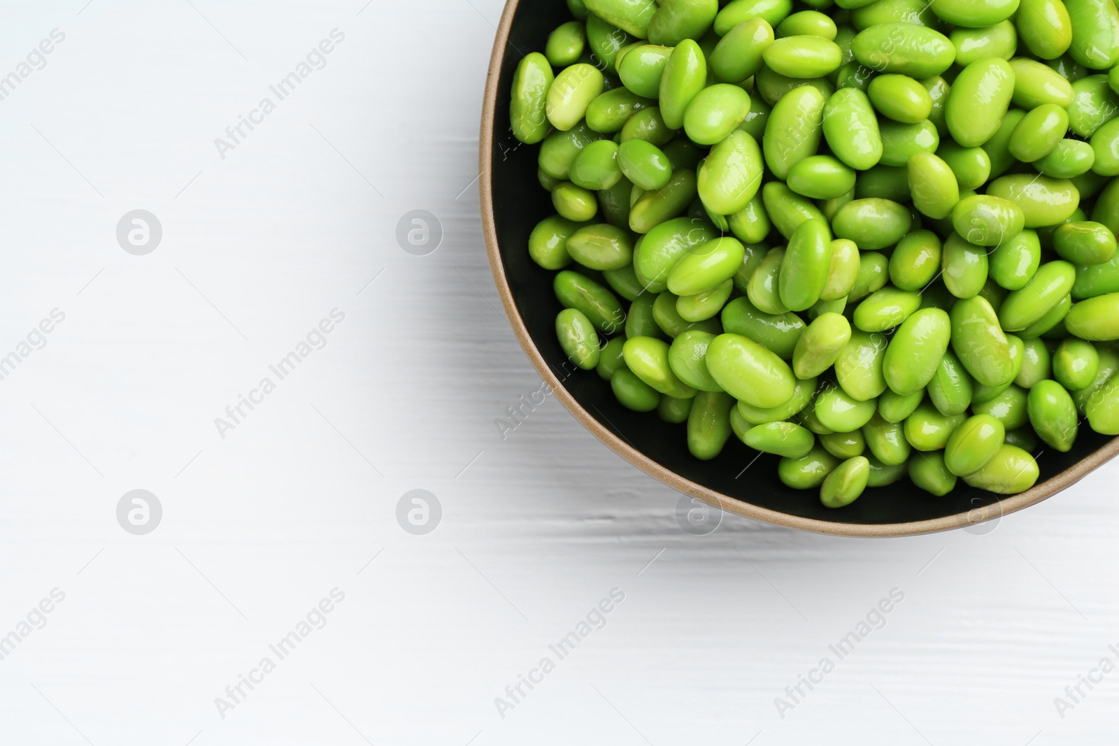 Photo of Fresh edamame soybeans in bowl on white wooden table, top view. Space for text