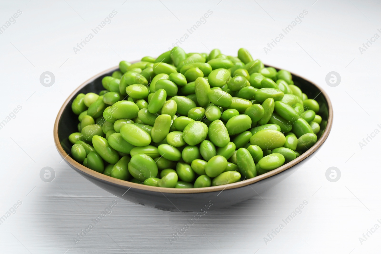 Photo of Fresh edamame soybeans in bowl on white wooden table, closeup