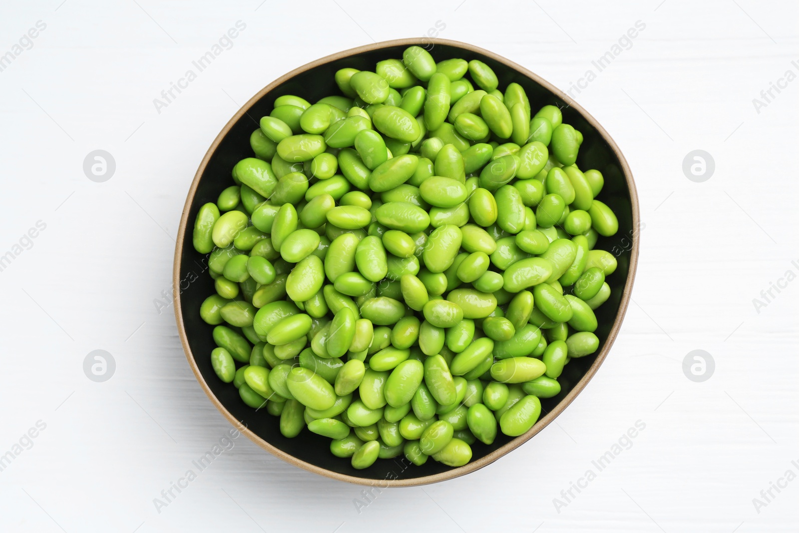 Photo of Fresh edamame soybeans in bowl on white wooden table, top view