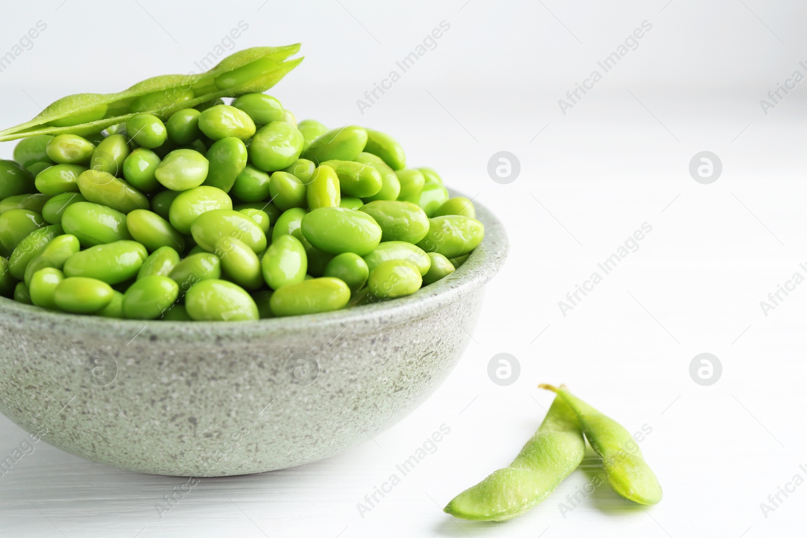 Photo of Fresh edamame soybeans in bowl and pods on white wooden table, closeup