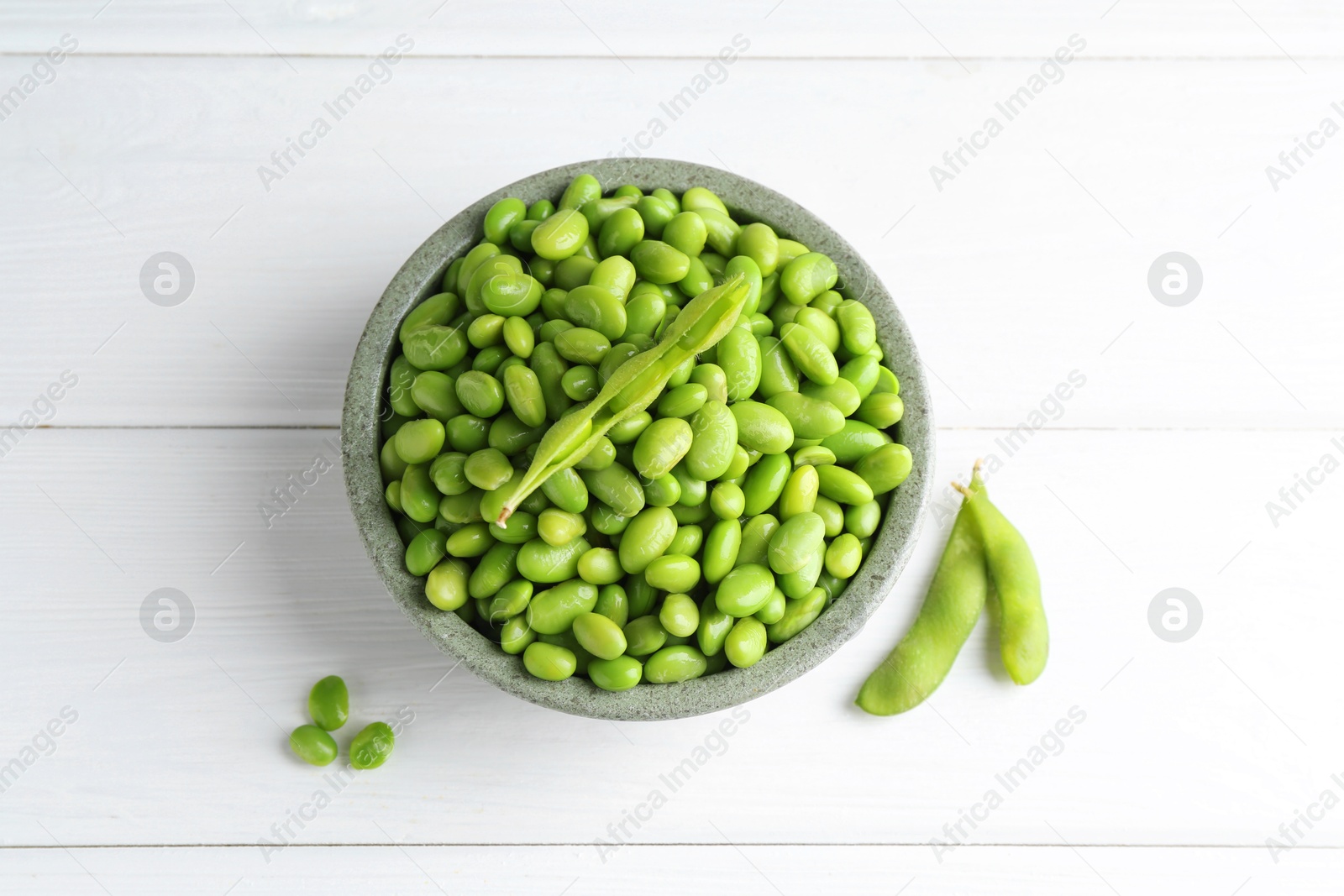 Photo of Fresh edamame soybeans in bowl and pods on white wooden table, flat lay