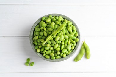 Fresh edamame soybeans in bowl and pods on white wooden table, flat lay