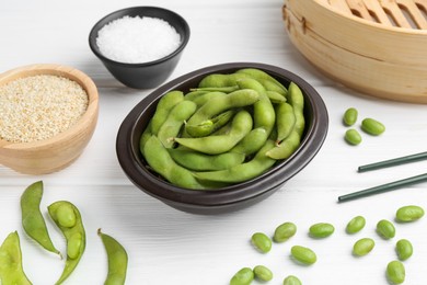 Photo of Fresh edamame pods, soybeans, salt and seeds on white wooden table, closeup