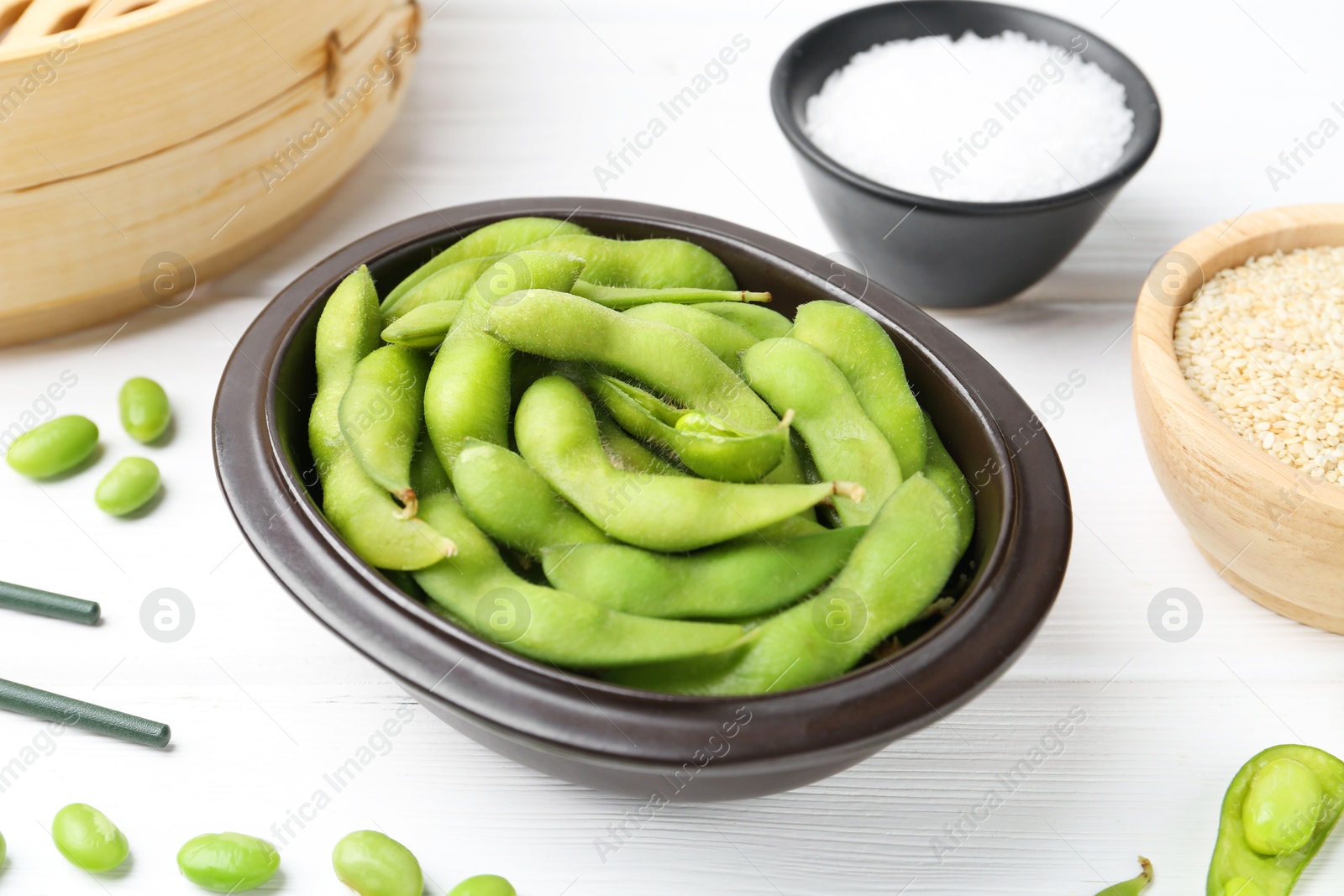 Photo of Fresh edamame pods, soybeans, salt and seeds on white wooden table, closeup