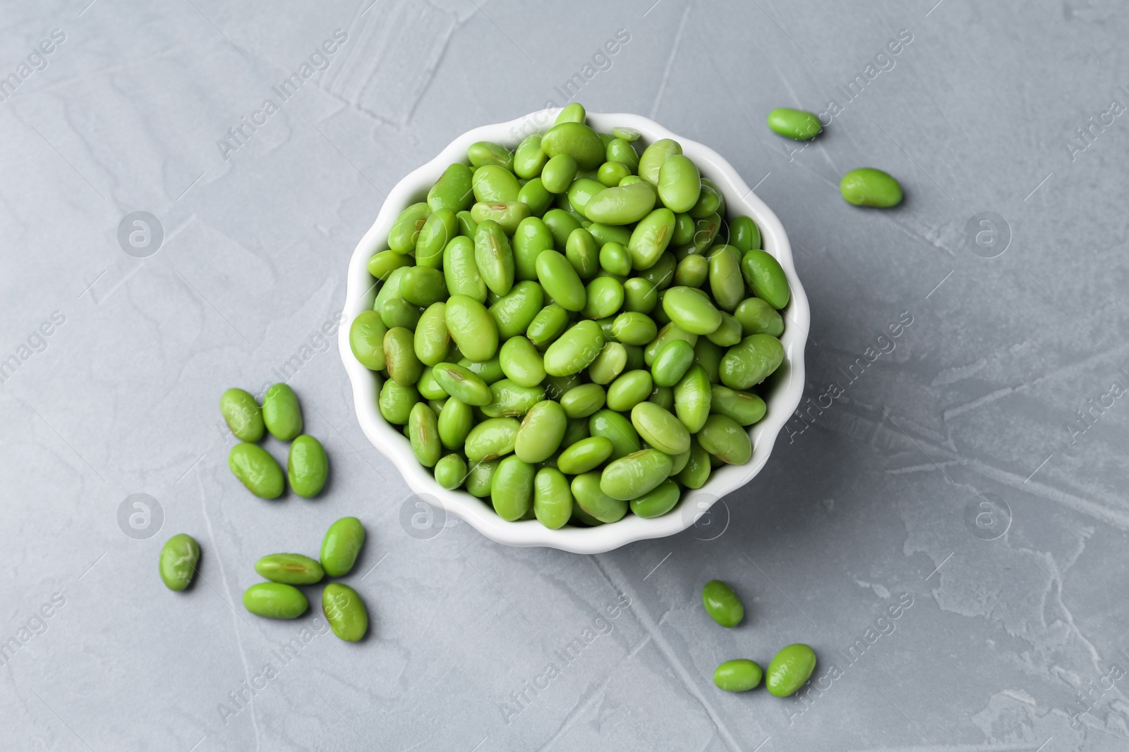 Photo of Fresh edamame soybeans in bowl on grey textured table, top view