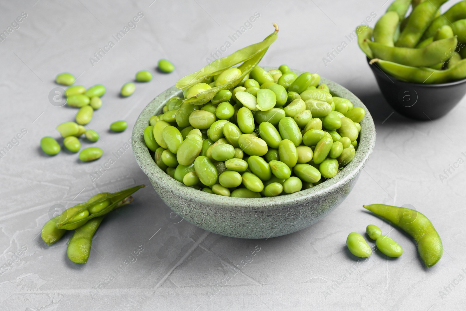 Photo of Fresh edamame soybeans in bowl and pods on grey textured table, closeup