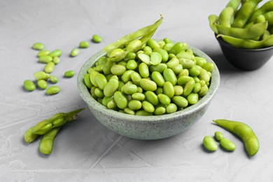 Fresh edamame soybeans in bowl and pods on grey textured table, closeup