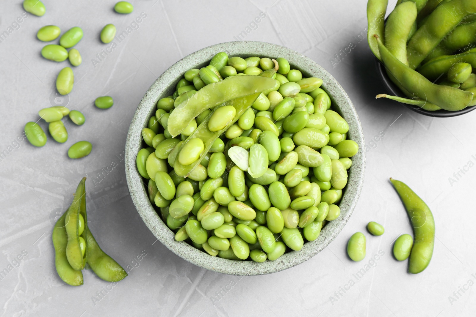 Photo of Fresh edamame soybeans in bowl and pods on grey textured table, flat lay