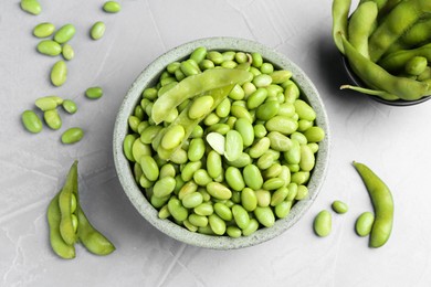 Fresh edamame soybeans in bowl and pods on grey textured table, flat lay