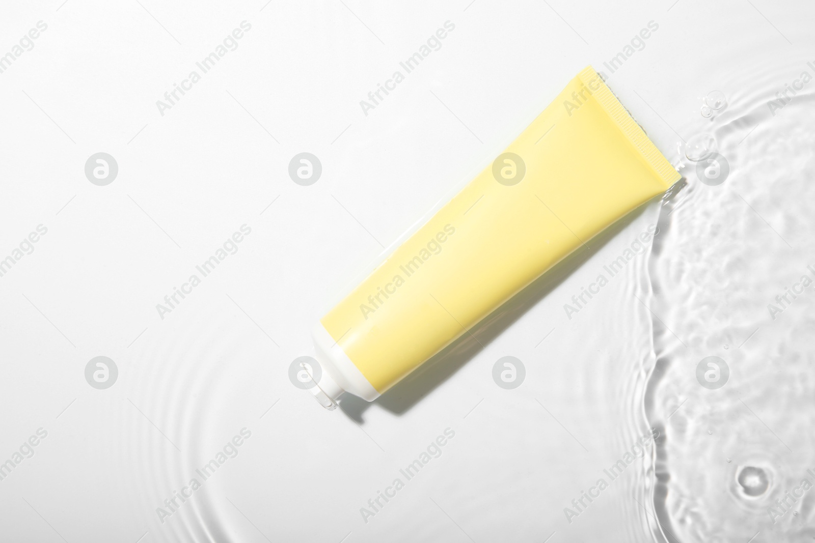 Photo of Cosmetic product. Tube with cream in water on light background, top view