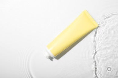 Photo of Cosmetic product. Tube with cream in water on light background, top view