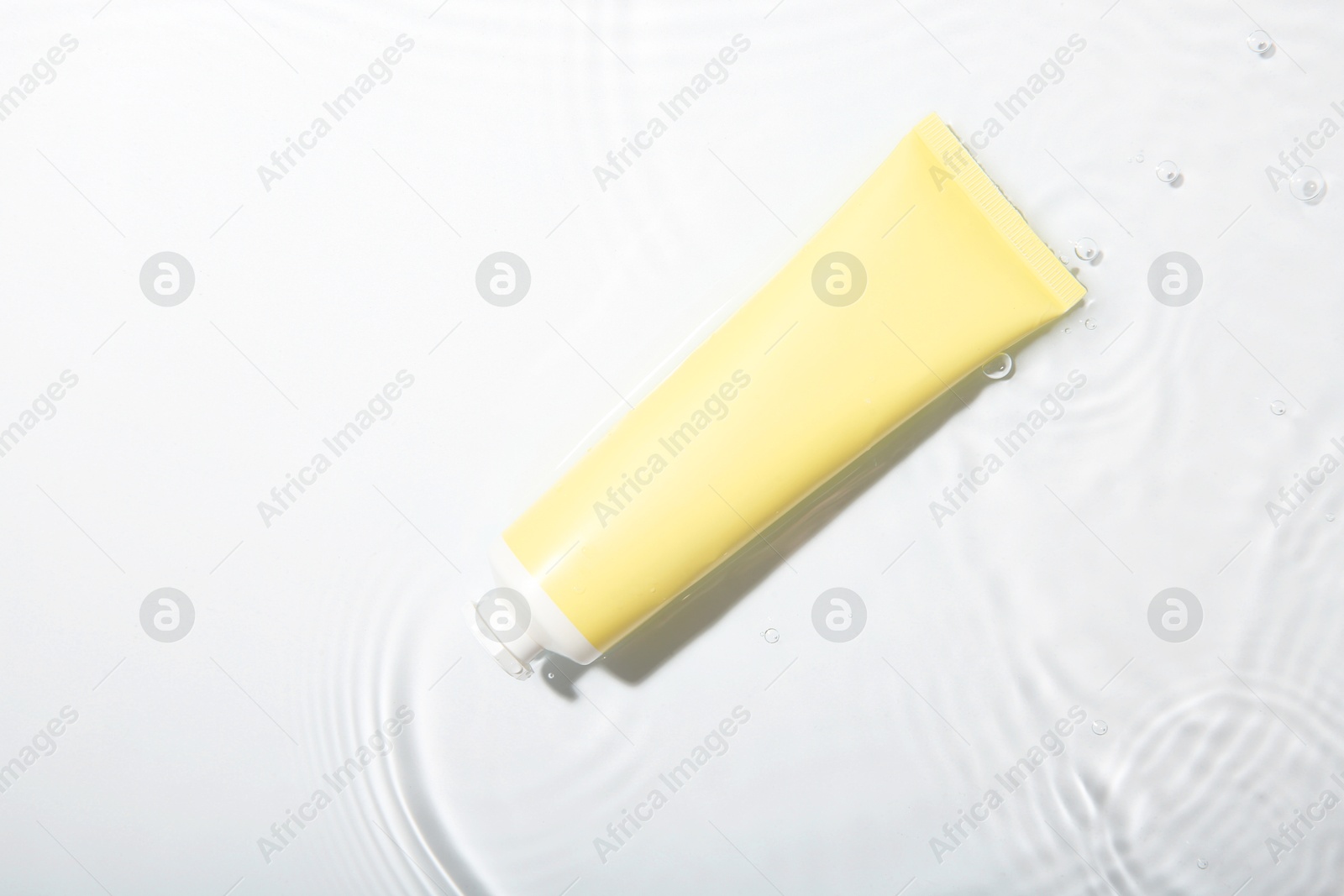 Photo of Cosmetic product. Tube with cream in water on light background, top view