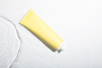 Photo of Cosmetic product. Tube with cream in water on light background, top view