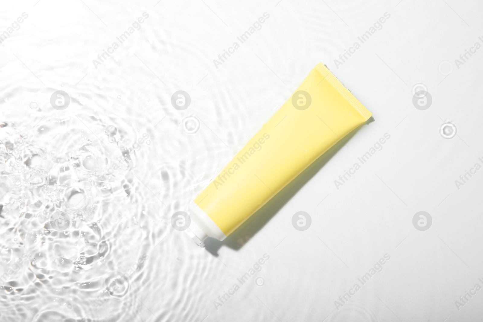 Photo of Cosmetic product. Tube with cream in water on light background, top view