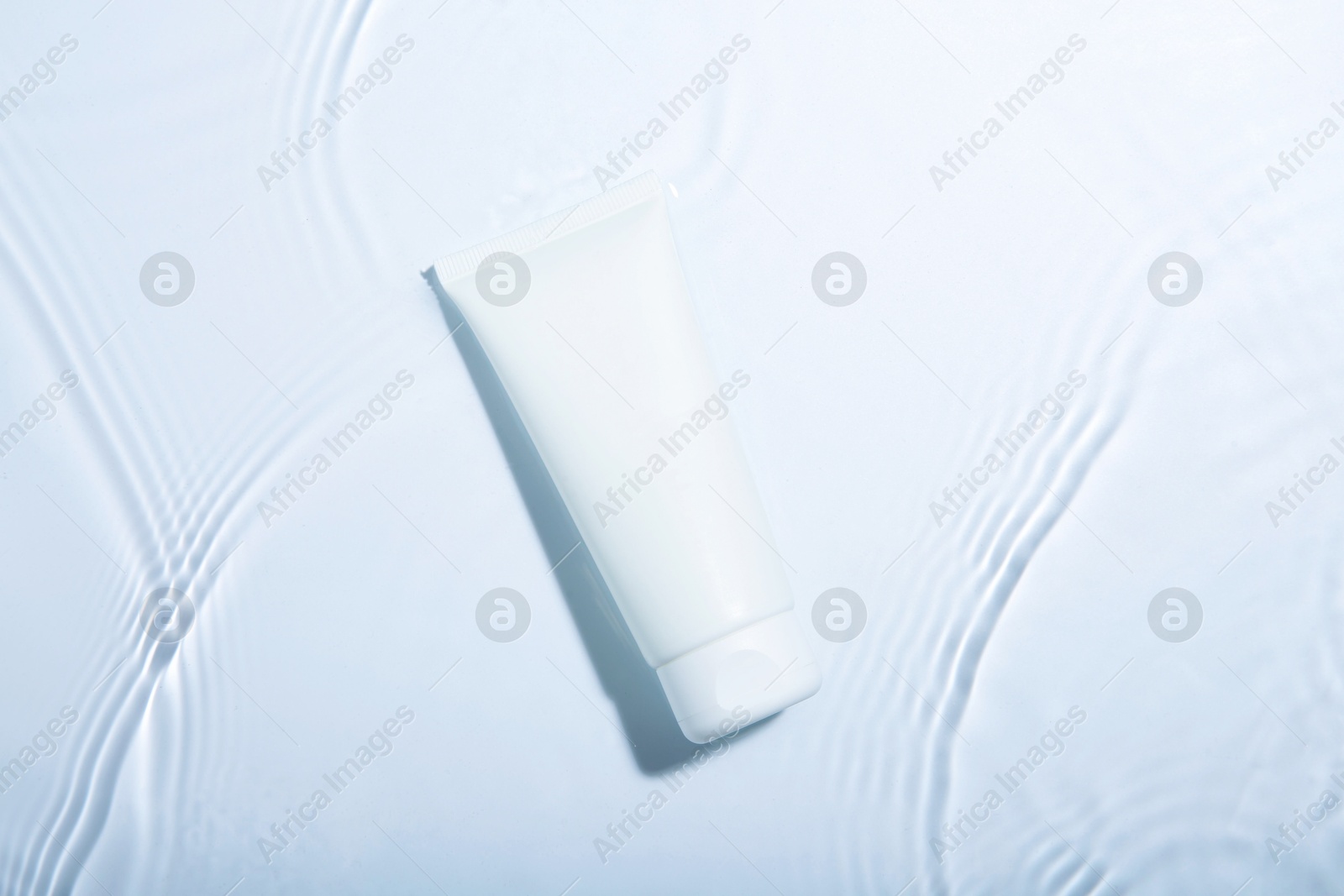 Photo of Cosmetic product. Tube with cream in water on light background, top view