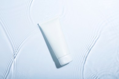 Photo of Cosmetic product. Tube with cream in water on light background, top view