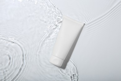 Cosmetic product. Tube with cream in water on light background, top view