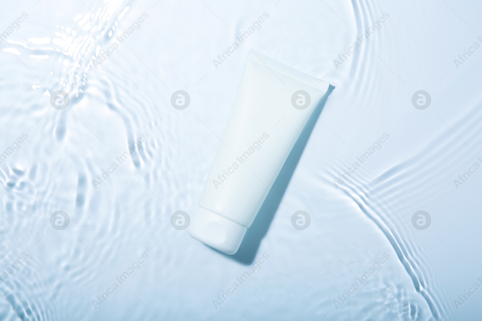 Photo of Cosmetic product. Tube with cream in water on light background, top view