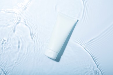 Cosmetic product. Tube with cream in water on light background, top view