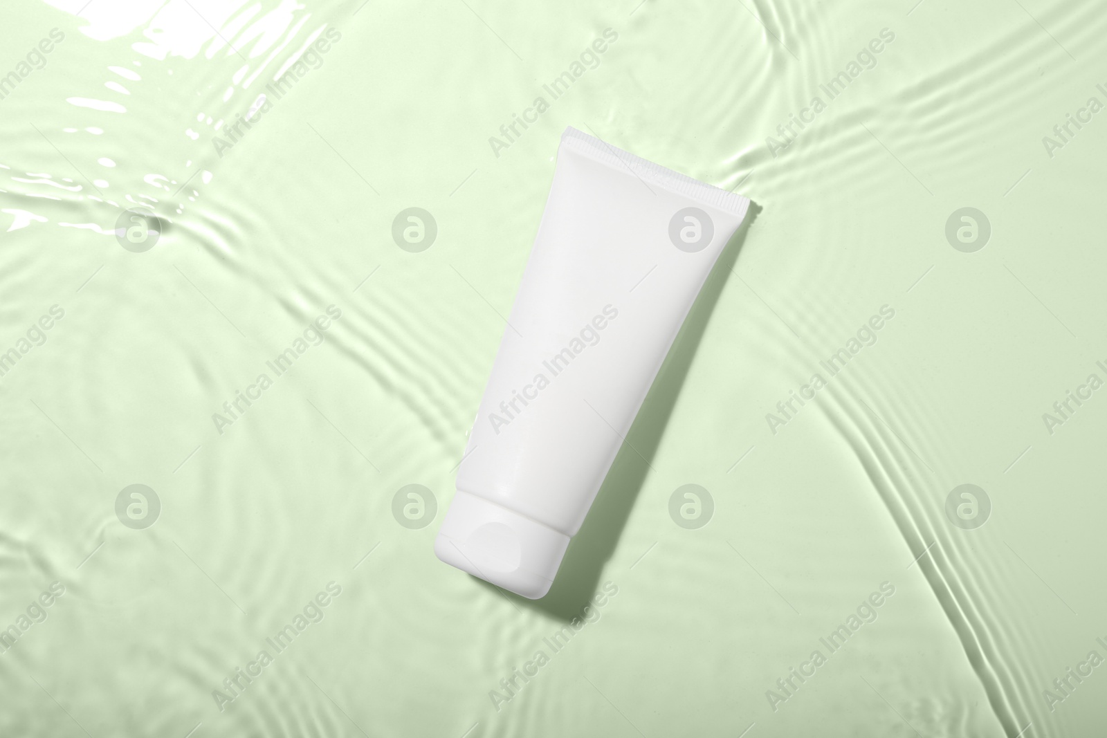 Photo of Cosmetic product. Tube with cream in water on light background, top view