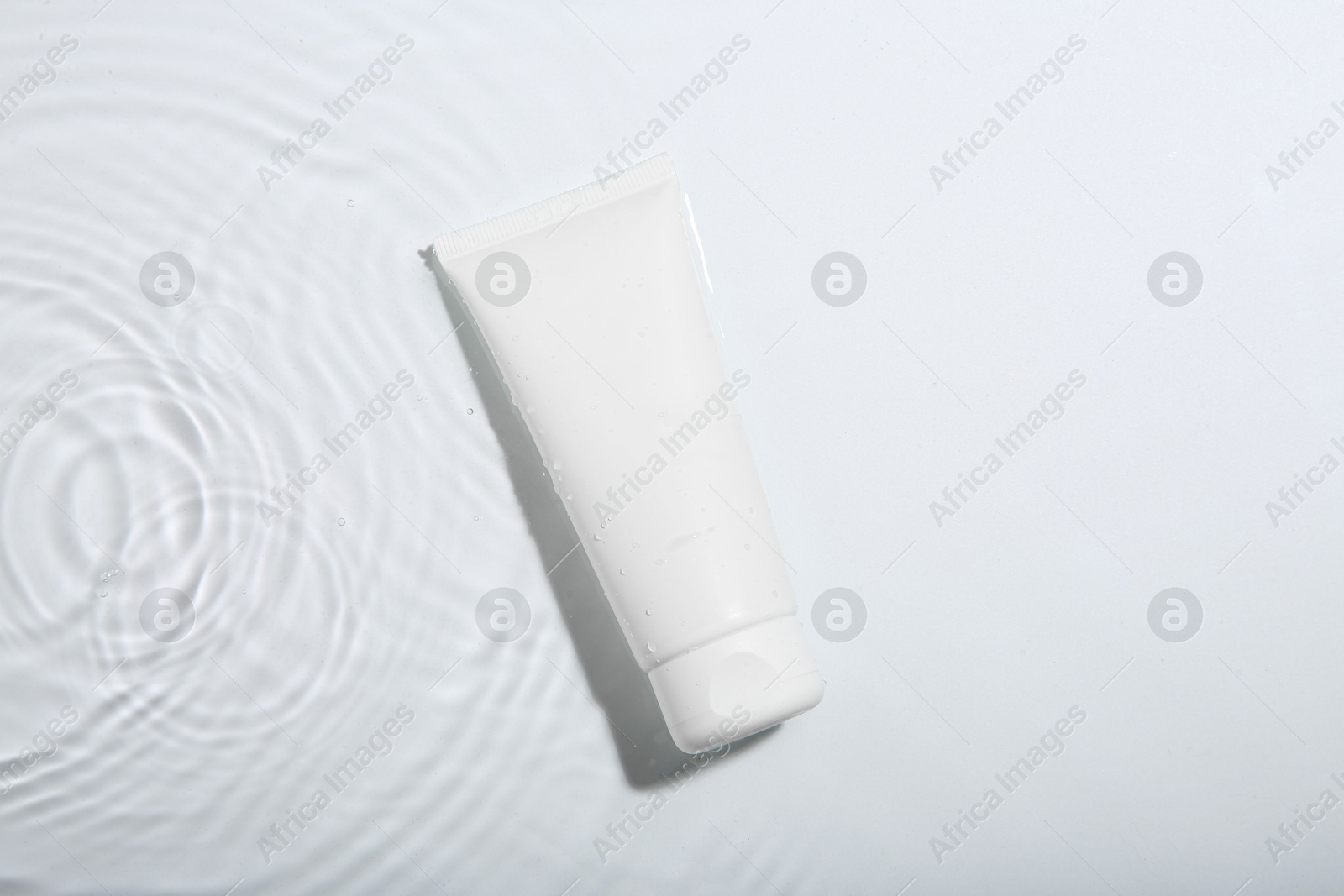 Photo of Cosmetic product. Tube with cream in water on light background, top view