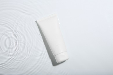 Photo of Cosmetic product. Tube with cream in water on light background, top view