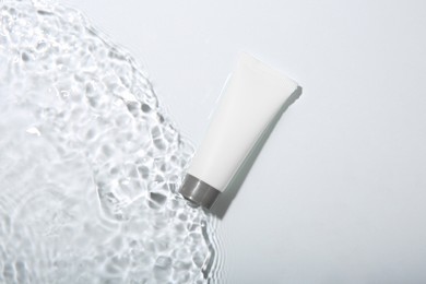 Photo of Cosmetic product. Tube with cream in water on light background, top view