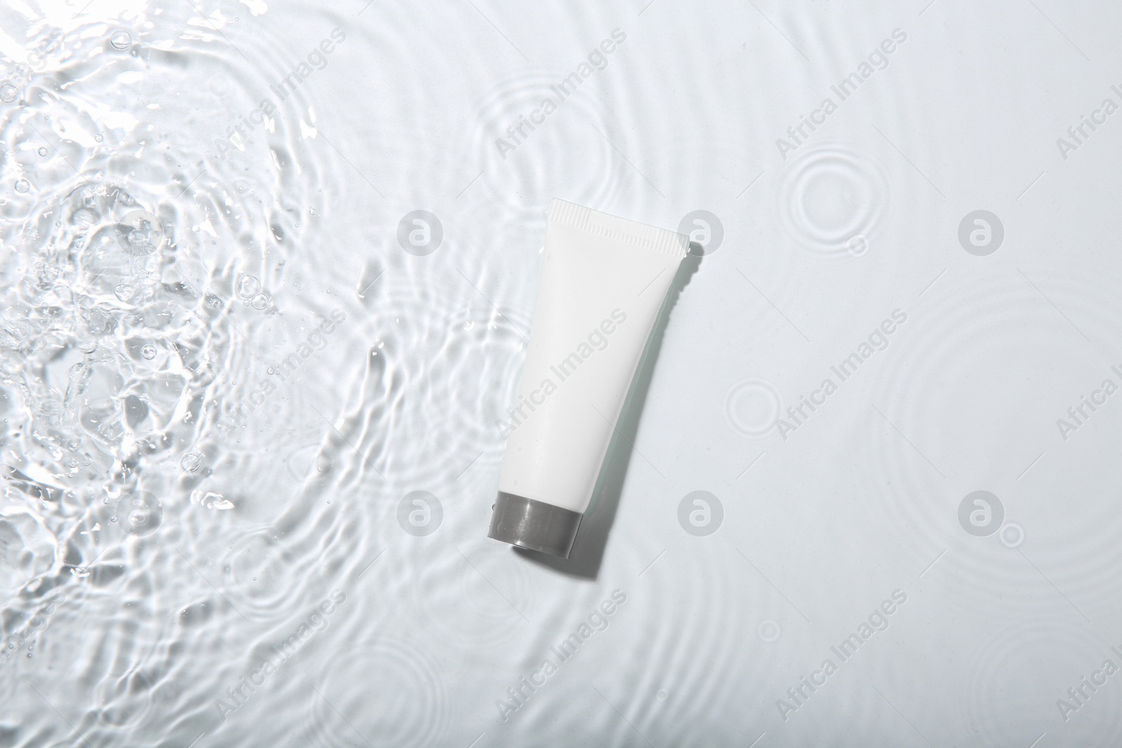 Photo of Cosmetic product. Tube with cream in water on light background, top view