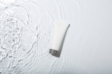 Cosmetic product. Tube with cream in water on light background, top view