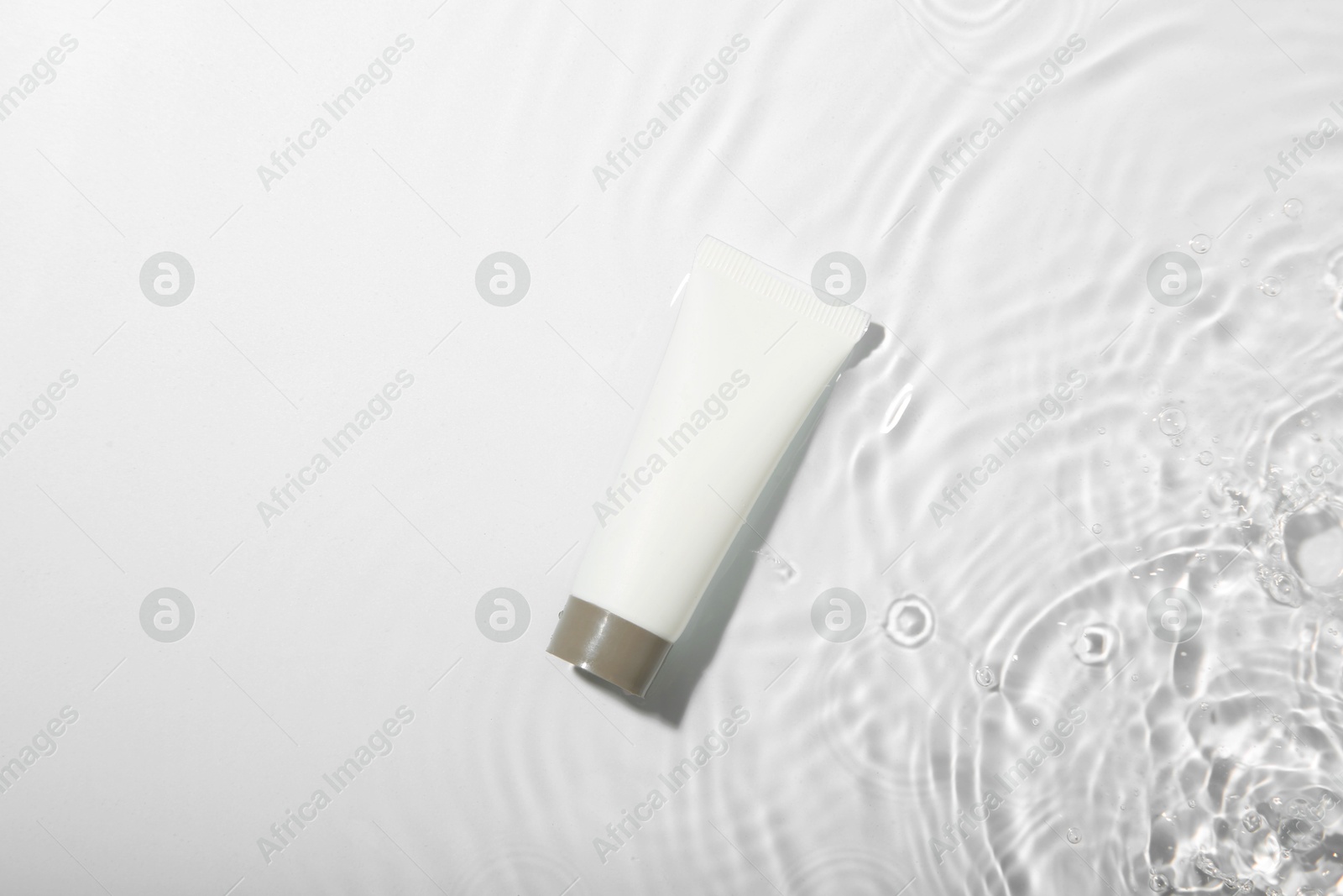 Photo of Cosmetic product. Tube with cream in water on light background, top view