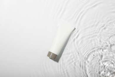 Photo of Cosmetic product. Tube with cream in water on light background, top view