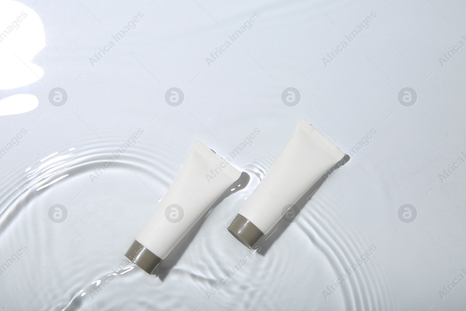 Photo of Cosmetic products. Tubes with cream in water on light background, top view