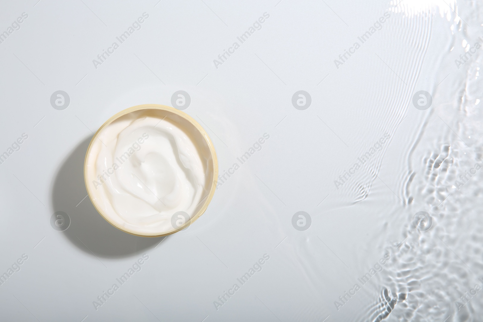 Photo of Cosmetic product. Jar with cream in water on light background, top view. Space for text