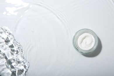 Photo of Cosmetic product. Jar with cream in water on light background, top view. Space for text