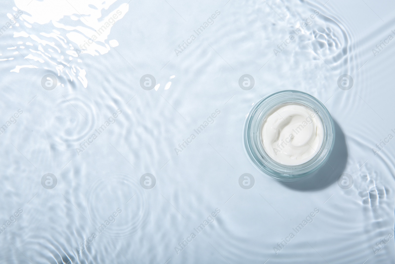 Photo of Cosmetic product. Jar with cream in water on light background, top view. Space for text