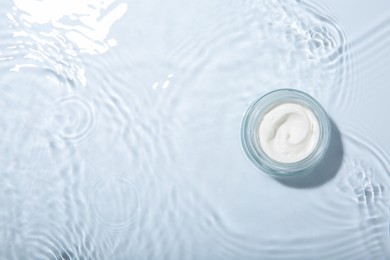 Photo of Cosmetic product. Jar with cream in water on light background, top view. Space for text