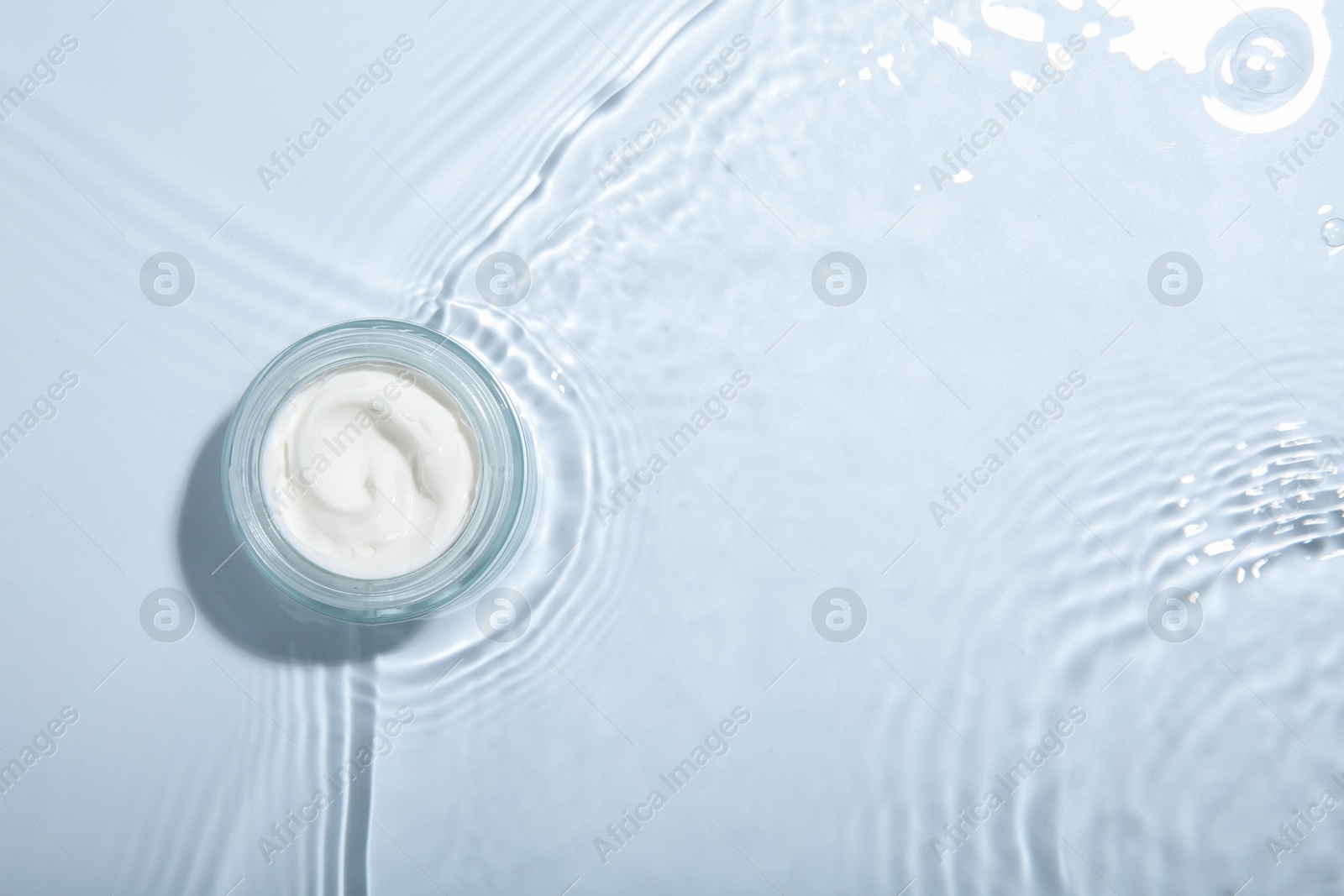 Photo of Cosmetic product. Jar with cream in water on light background, top view. Space for text