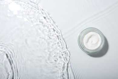 Photo of Cosmetic product. Jar with cream in water on light background, top view. Space for text