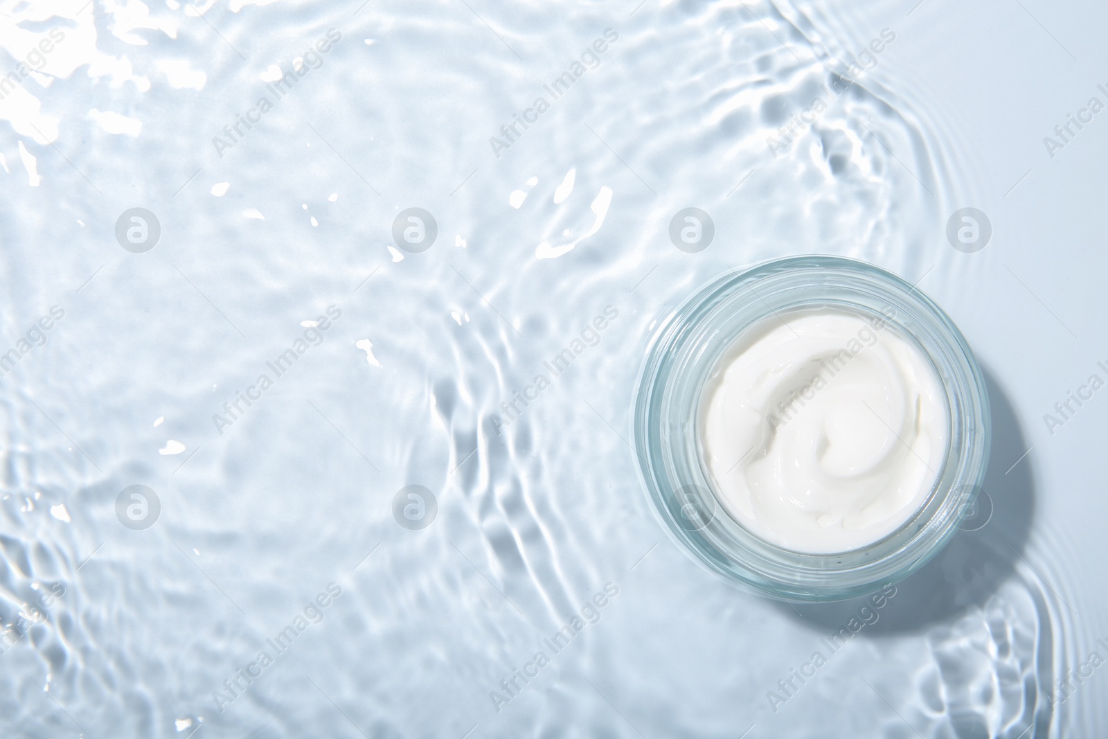 Photo of Cosmetic product. Jar with cream in water on light background, top view. Space for text