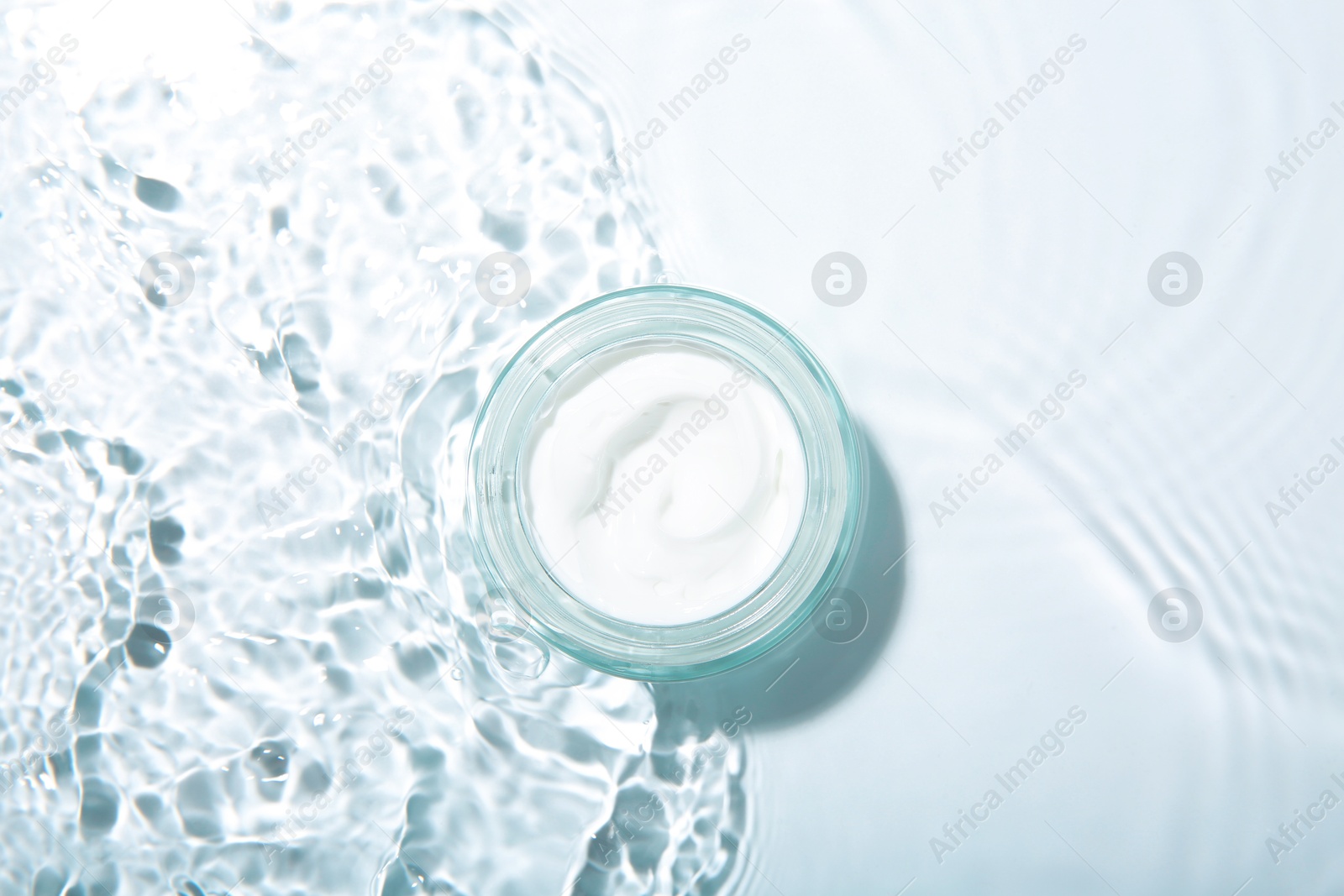 Photo of Cosmetic product. Jar with cream in water on light background, top view