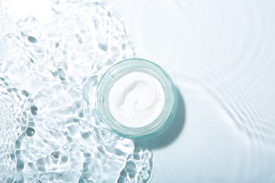 Photo of Cosmetic product. Jar with cream in water on light background, top view