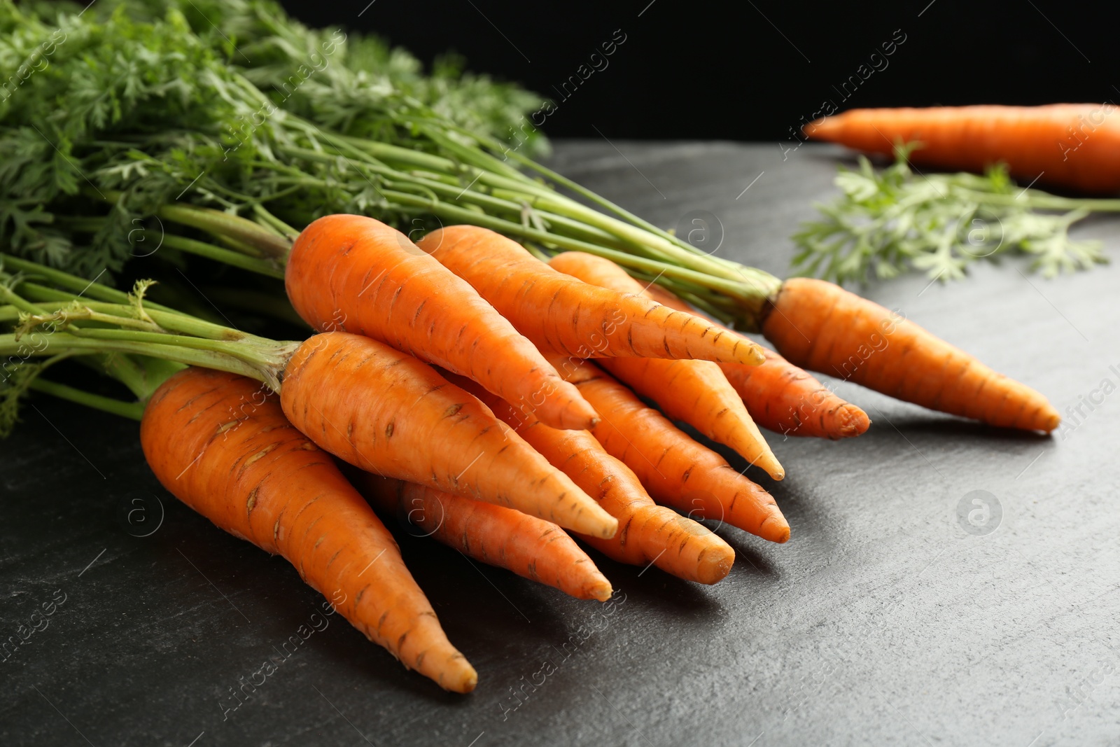 Photo of Tasty ripe juicy carrots on dark gray textured table, closeup