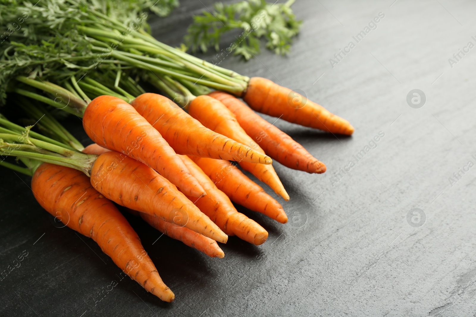 Photo of Tasty ripe juicy carrots on dark gray textured table, closeup