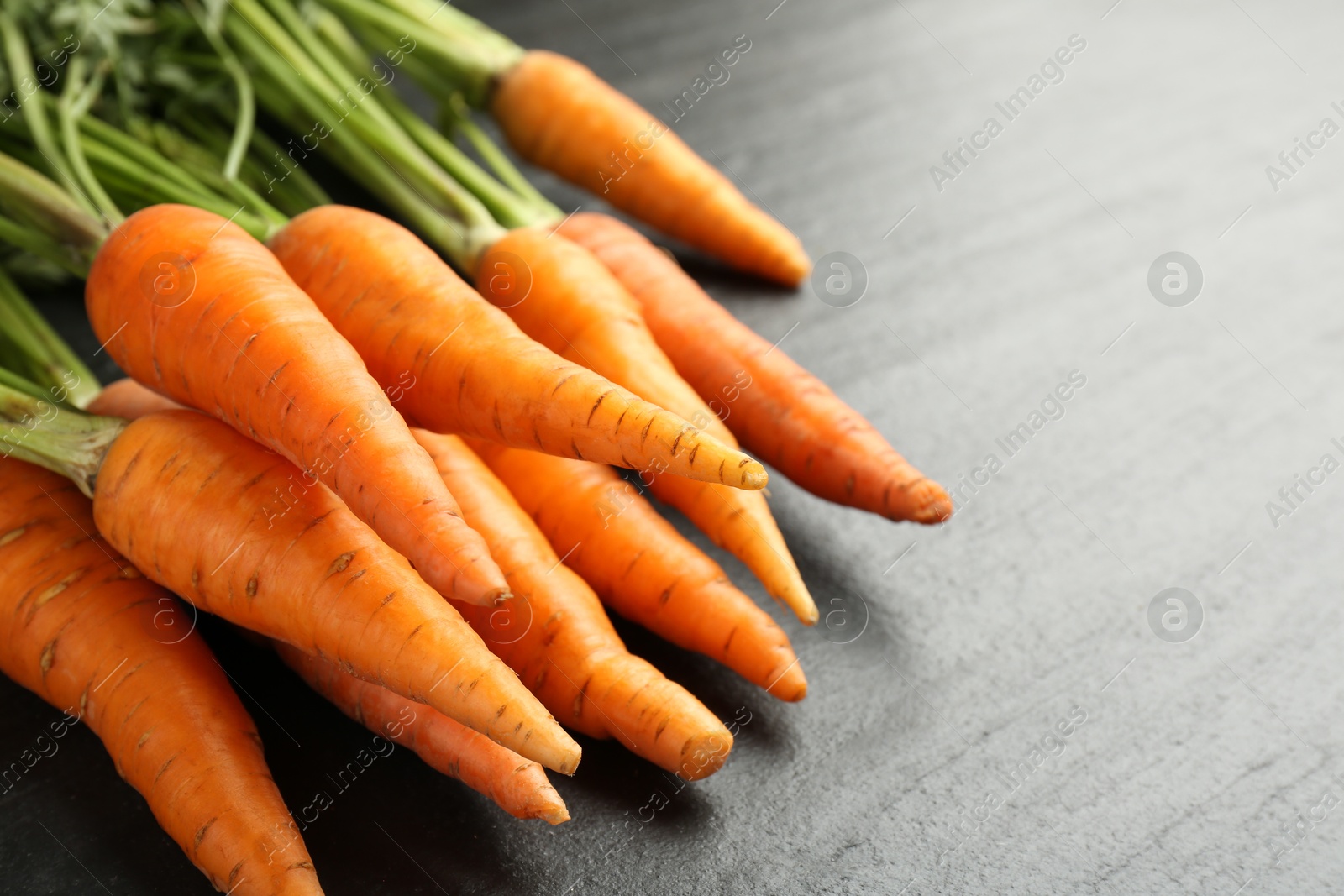 Photo of Tasty ripe juicy carrots on dark gray textured table, closeup