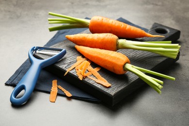 Photo of Fresh carrots, vegetable peeler and peels on gray textured table, closeup